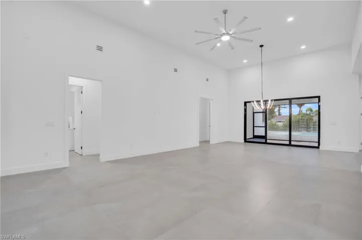 Empty room with a high ceiling, ceiling fan with notable chandelier, and tile flooring