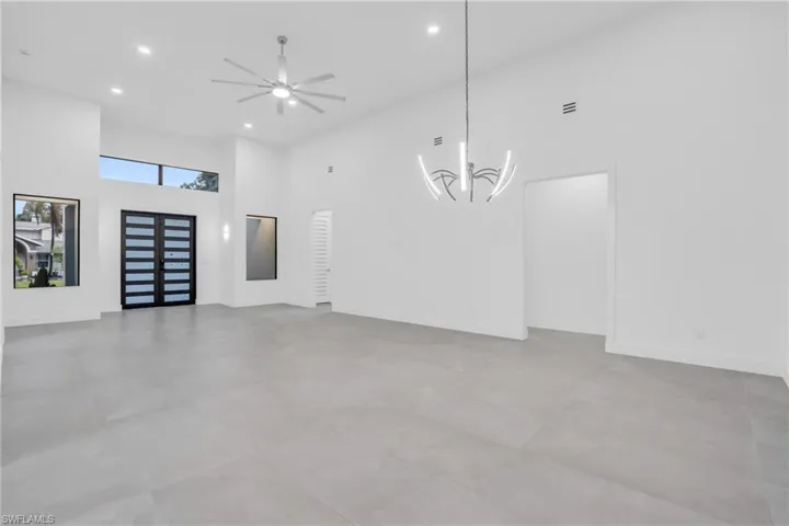 Unfurnished living room featuring a towering ceiling, tile floors, and ceiling fan with notable chandelier
