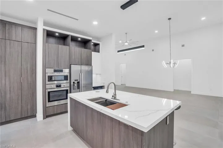 Kitchen featuring ceiling fan with notable chandelier, appliances with stainless steel finishes, a kitchen island with sink, light stone counters, and sink