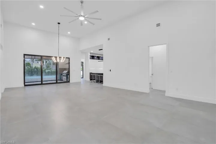 Unfurnished living room featuring a high ceiling, ceiling fan with notable chandelier, and tile floors