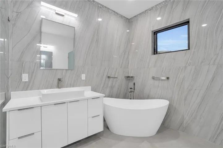 Primary bathroom featuring tile walls, tile floors, separate vanity and soaking tub