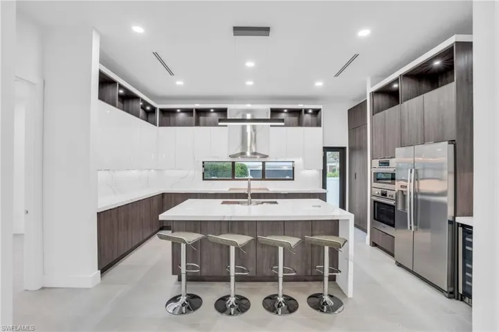 Kitchen featuring light  quartz counters, stainless steel appliances, backsplash, a kitchen island with sink, and a kitchen bar