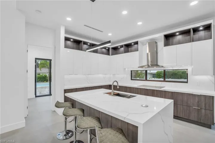Kitchen with decorative light fixtures, white cabinetry, a kitchen island with sink, and wall chimney exhaust hood