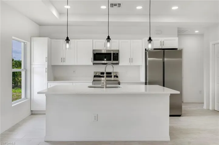 Kitchen featuring appliances with stainless steel finishes, white cabinetry, an island with sink, and pendant lighting