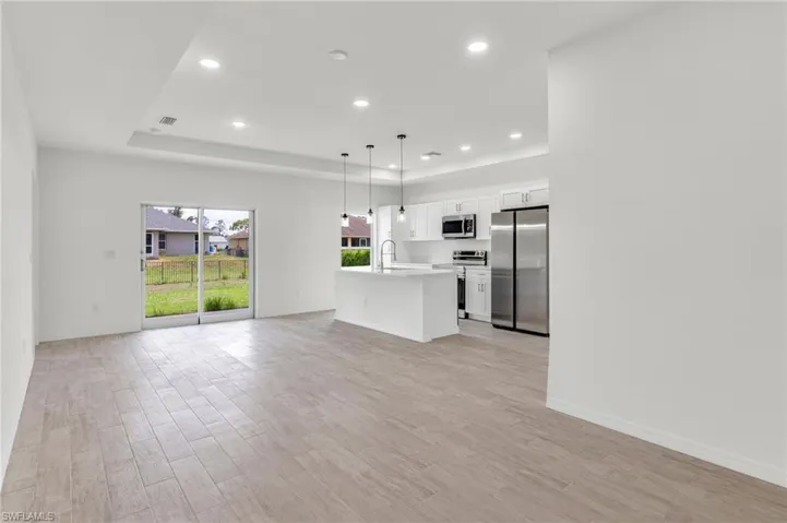 Unfurnished living room featuring a raised ceiling, sink, and light wood-type flooring