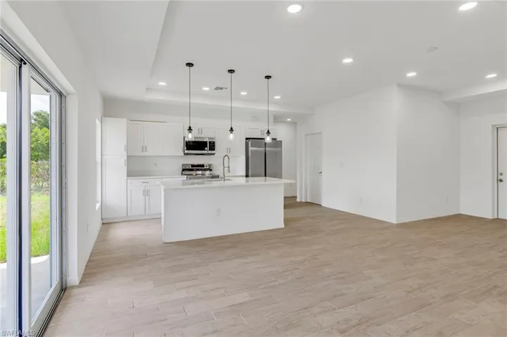 Kitchen featuring light hardwood / wood-style floors, hanging light fixtures, a center island with sink, white cabinetry, and appliances with stainless steel finishes
