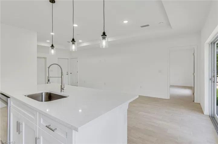 Kitchen with sink, white cabinets, a center island with sink, and hanging light fixtures