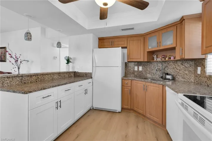 Kitchen featuring a raised ceiling, white appliances, stacked washer / dryer, and light wood-style floors