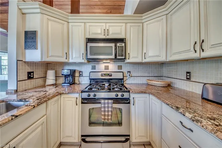 Kitchen featuring decorative backsplash, light stone countertops, cream cabinets, and stainless steel appliances