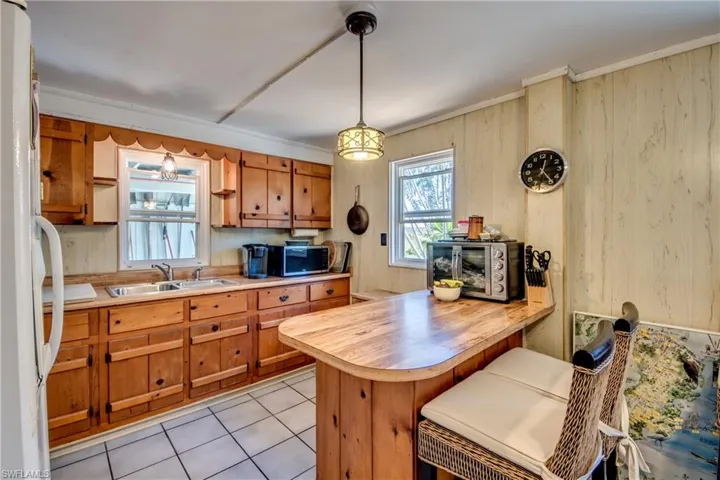Kitchen with a breakfast bar, sink, light tile patterned floors, hanging light fixtures, and kitchen peninsula