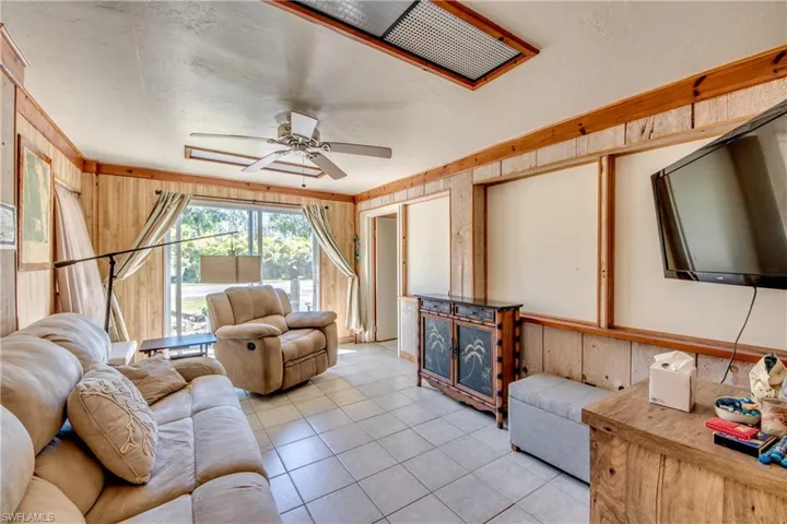 Living room with ceiling fan, light tile patterned floors, and wooden walls