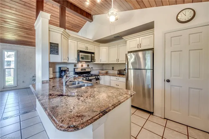 Kitchen featuring vaulted ceiling with beams, appliances with stainless steel finishes, light tile patterned floors, wood ceiling, and kitchen peninsula