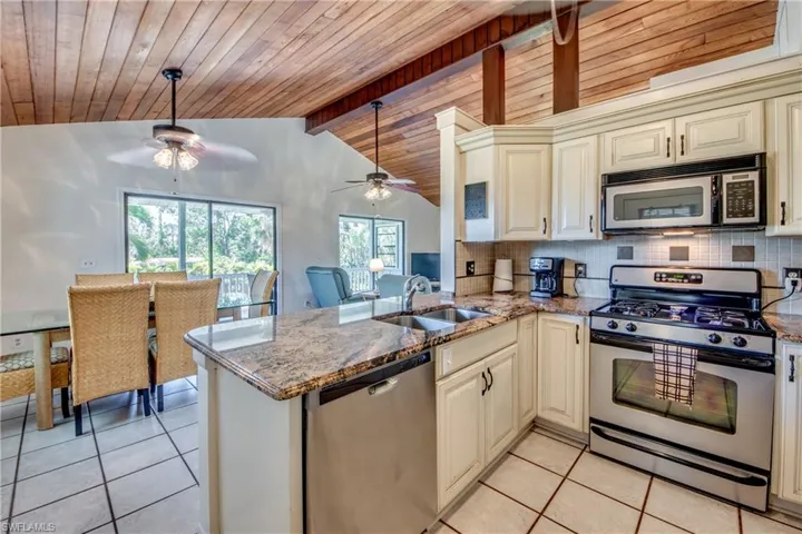 Kitchen featuring appliances with stainless steel finishes, ceiling fan, lofted ceiling with beams, and kitchen peninsula