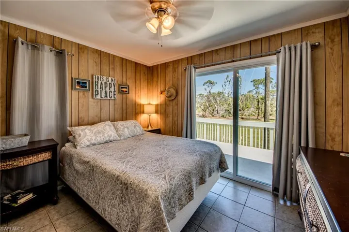 Tiled bedroom featuring ceiling fan, wooden walls, access to outside, and crown molding