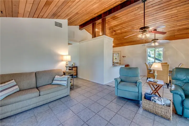 Tiled living room featuring ceiling fan, vaulted ceiling with beams, and wooden ceiling