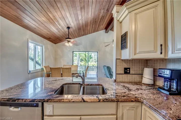 Kitchen with ceiling fan, dishwasher, lofted ceiling, and stone counters