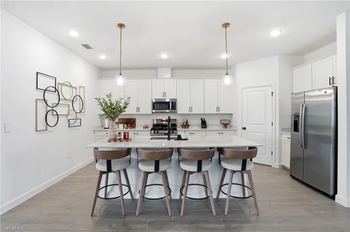Kitchen with appliances with stainless steel finishes, hanging light fixtures, a kitchen island with sink, light wood-type flooring, and white cabinets