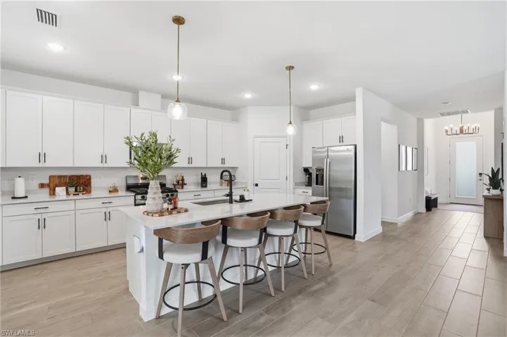 Kitchen featuring stainless steel appliances, a breakfast bar, decorative light fixtures, light wood-style flooring, and an island with sink