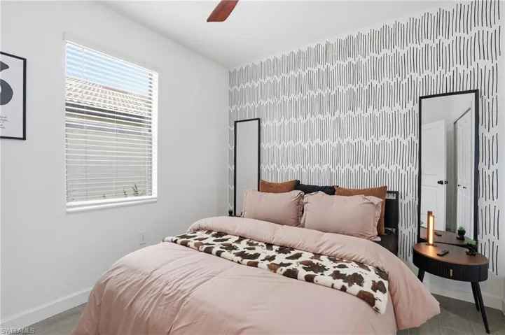 Bedroom featuring an accent wall, wallpapered walls, wood finished floors, and a ceiling fan