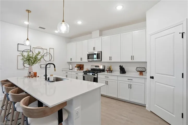 Kitchen featuring appliances with stainless steel finishes, pendant lighting, white cabinetry, a breakfast bar, and light wood-style flooring