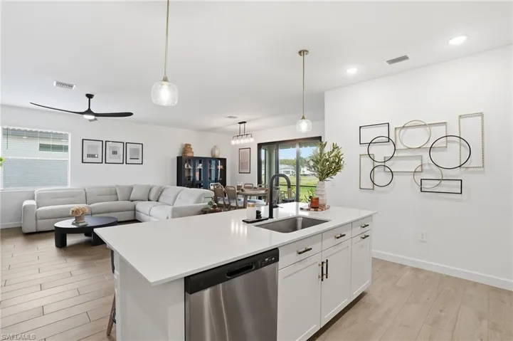 Kitchen with stainless steel dishwasher, white cabinets, wood finish floors, ceiling fan, and a center island with sink