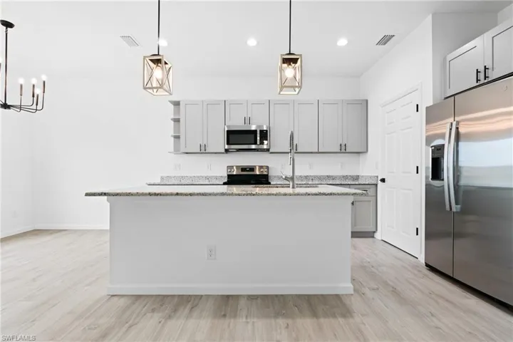 stainless steel finishes, light stone countertops, and a kitchen island with sink