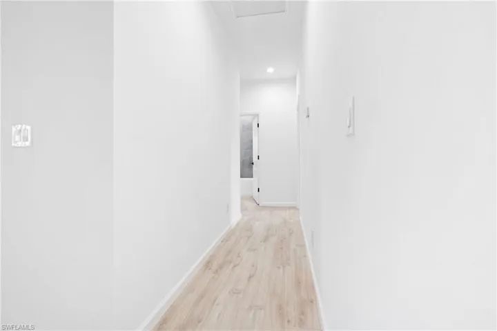 Hallway with light wood-type flooring and recessed lighting