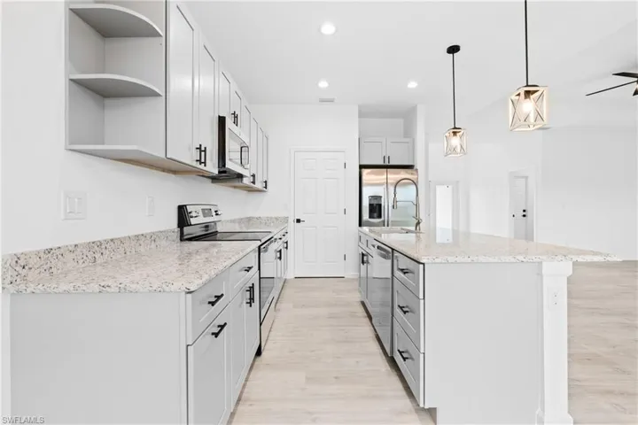 Kitchen with stainless steel appliances, open shelves, light stone counters, hanging light fixtures, and recessed lighting