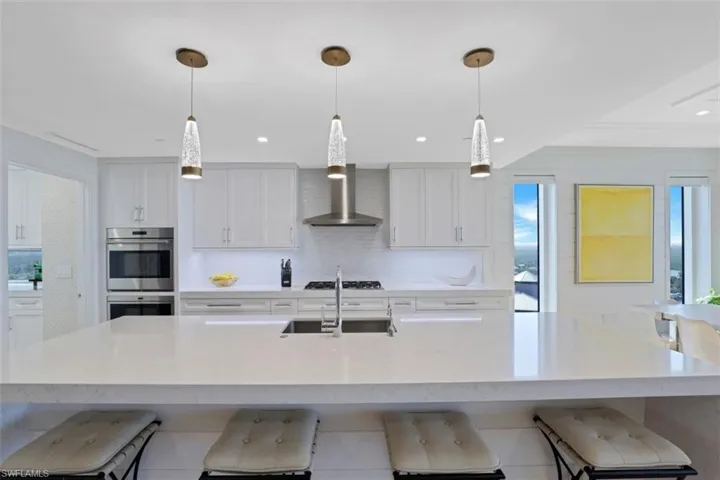 Kitchen with a kitchen bar, stainless steel double oven, white cabinets, decorative backsplash, and a large island