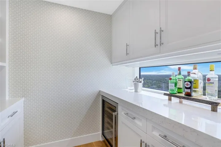 Indoor dry bar with wallpapered walls, beverage cooler, and light wood-style floors
