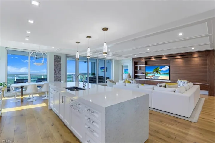 Kitchen featuring white cabinetry, light wood finished floors, an island with sink, light stone counters, and open floor plan