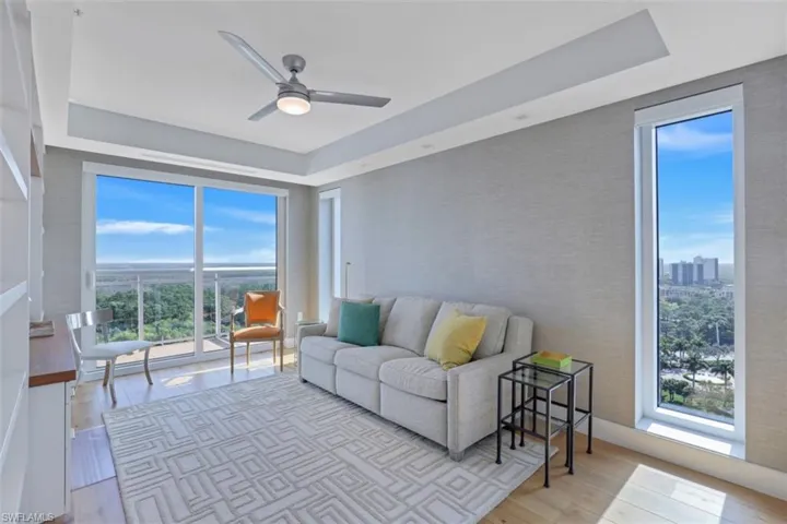 Living area with a raised ceiling, plenty of natural light, ceiling fan, and wood finished floors