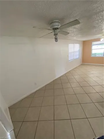 Empty room with ceiling fan, a textured ceiling, and light tile floors