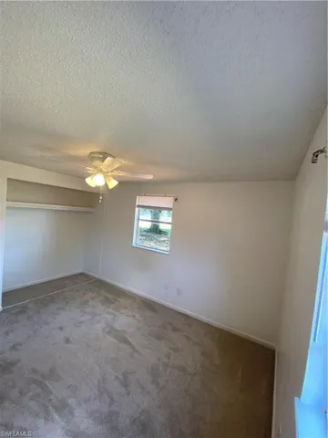Carpeted empty room featuring a textured ceiling and ceiling fan