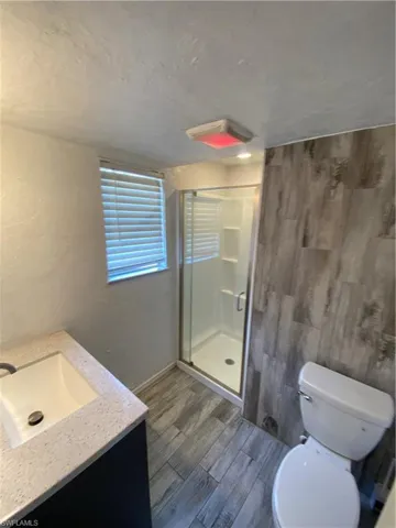 Bathroom with hardwood / wood-style floors, a shower with shower door, toilet, and vanity