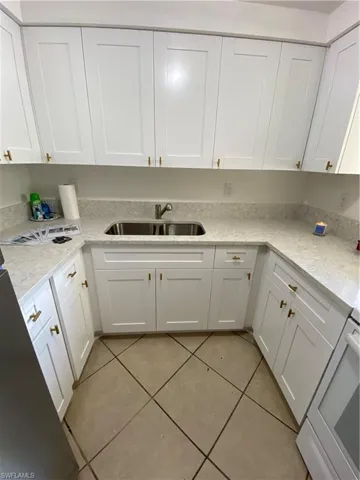 Kitchen with stove, light stone counters, light tile floors, sink, and white cabinets