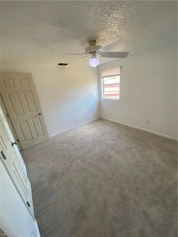 Carpeted empty room with ceiling fan and a textured ceiling