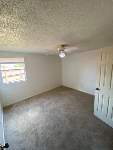 Spare room with a textured ceiling, ceiling fan, and dark carpet