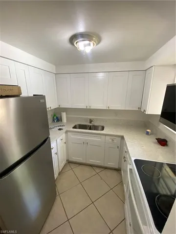 Kitchen featuring range, light tile floors, sink, white cabinets, and refrigerator