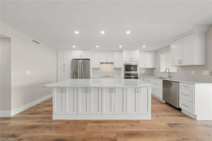 Kitchen featuring white cabinets, recessed lighting, light wood-type flooring, appliances with stainless steel finishes, and light stone counters