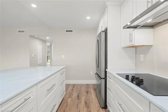 Kitchen with white cabinets, recessed lighting, wall chimney range hood, black electric stovetop, and light wood-style flooring