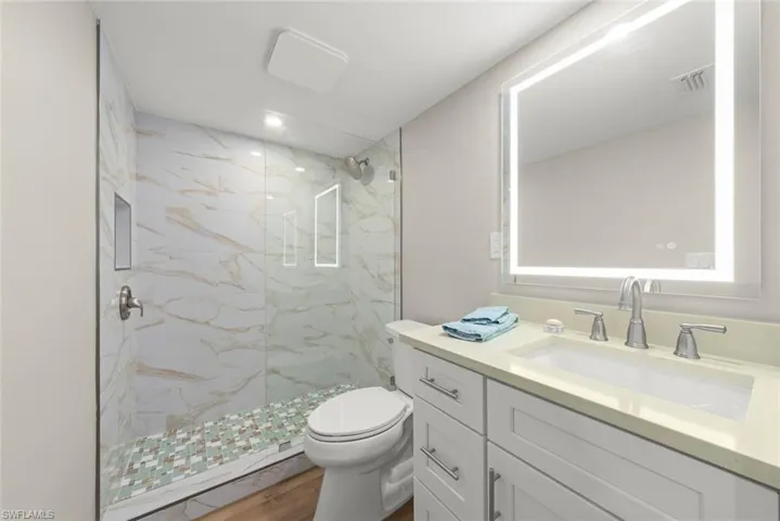 Full bath with a marble finish shower, vanity, and wood finished floors