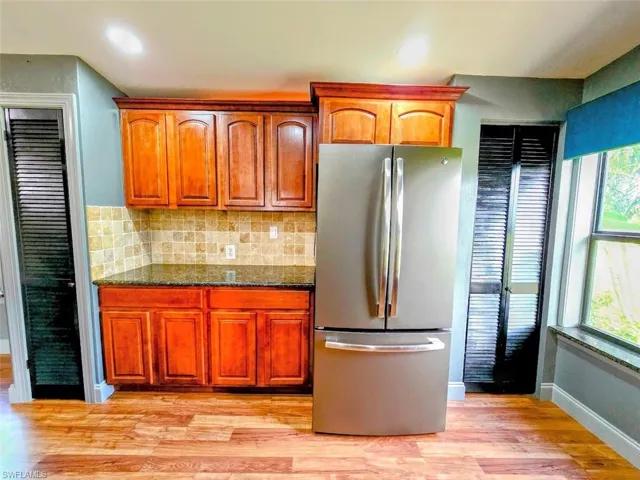 Kitchen featuring stainless steel fridge, light hardwood / wood-style floors, plenty of natural light, and dark stone counters