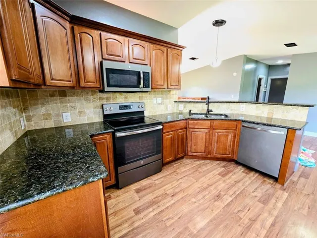 Kitchen with sink, light wood-type flooring, appliances with stainless steel finishes, and decorative backsplash