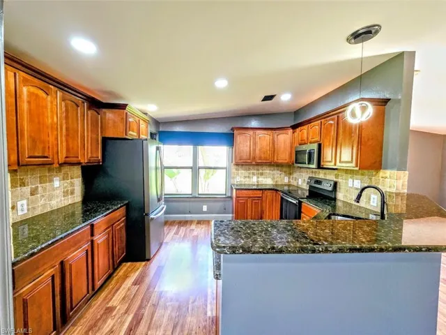 Kitchen with sink, hanging light fixtures, light wood-type flooring, stainless steel appliances, and kitchen peninsula