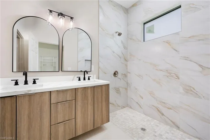Full bath featuring a marble finish shower and double vanity