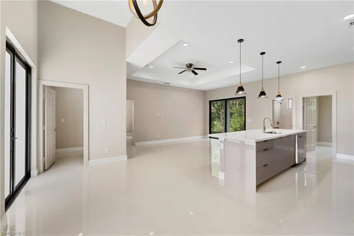 Kitchen featuring decorative light fixtures, a raised ceiling, a center island with sink, modern cabinets, and light stone counters