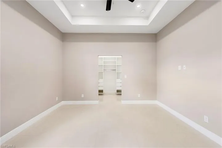 Unfurnished bedroom featuring a raised ceiling, a spacious closet, a ceiling fan, and recessed lighting
