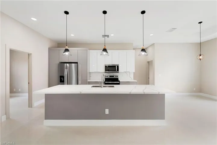 Kitchen with hanging light fixtures, stainless steel appliances, a center island with sink, light stone counters, and recessed lighting