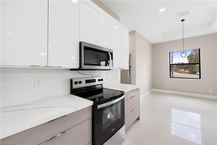 Kitchen with modern cabinets, appliances with stainless steel finishes, hanging light fixtures, white cabinets, and recessed lighting